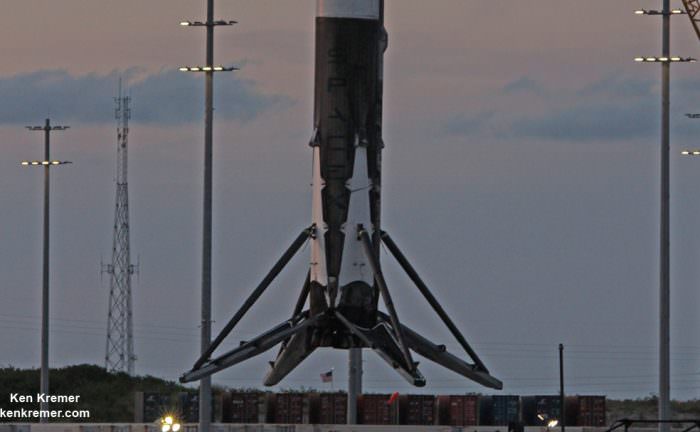 With US flag flying in background below, the base of recovered SpaceX Falcon 9 booster with 4 deployed landing legs and 9 Merlin 1 D engines is lifted off ‘OCISLY’ droneship barge at dusk on June 2, 2016 after sailing at  midday through Port Canaveral. The rocket  successfully launched Thaicom-8 satellite on May 27, 2016 from Cape Canaveral Air Force Station, Fl and landed on sea based platform minutes later.  Credit: Ken Kremer/kenkremer.com