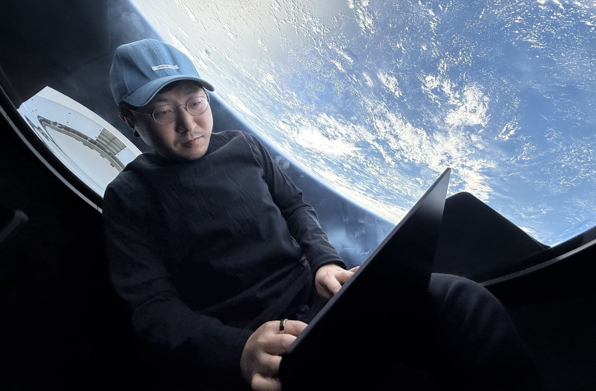 Mission commander Chun Wang works on his laptop with Earth looming outside the window of SpaceX's Dragon capsule during the Fram2 mission in 2025. (Chun Wang / SpaceX via X)