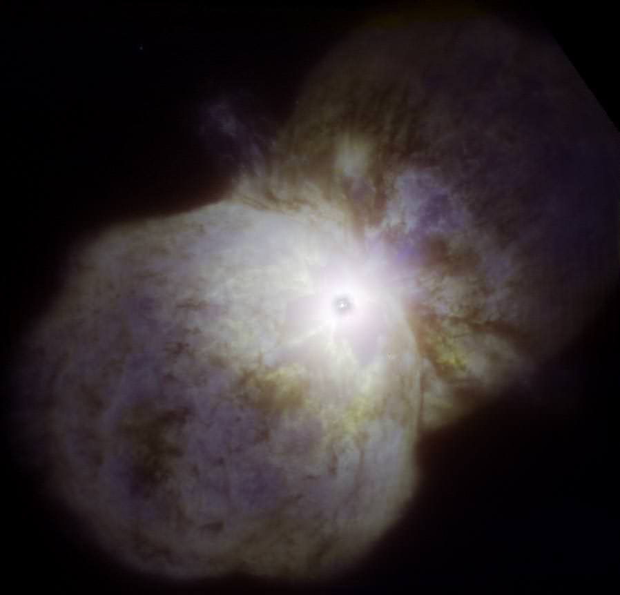 Eta Carinae as imaged by the Gemini South telescope in Chile with the Near Infrared Coronagraphic Imager (NICI) using adaptive optics to reduce blurring by turbulence in the Earth’s atmosphere. In this image the bipolar lobes of the Homunculus Nebula are visible with the never-before imaged “Little Homunculus Nebula” visible as a faint blue glow, mostly in the lower lobe. The Butterfly Nebula is visible (region circled) as the yellowish glow with dark filamentary structure close to, and mostly below/left, of the central star system (the central star system appears as a dark spot due to the coronagraphic blocking (occulting) disk used to eliminate the star’s bright glare).