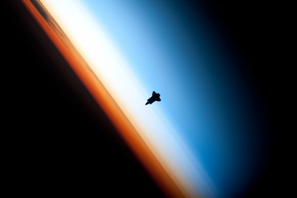 Космический корабль "Индевор" вырисовывался на фоне атмосферы.  Оранжевый слой — это тропосфера, белый — стратосфера, а синий — мезосфера.[1]  (На самом деле шаттл находится на высоте более 320 км (200 миль), намного выше всех трех слоев.) Предоставлено: НАСА.