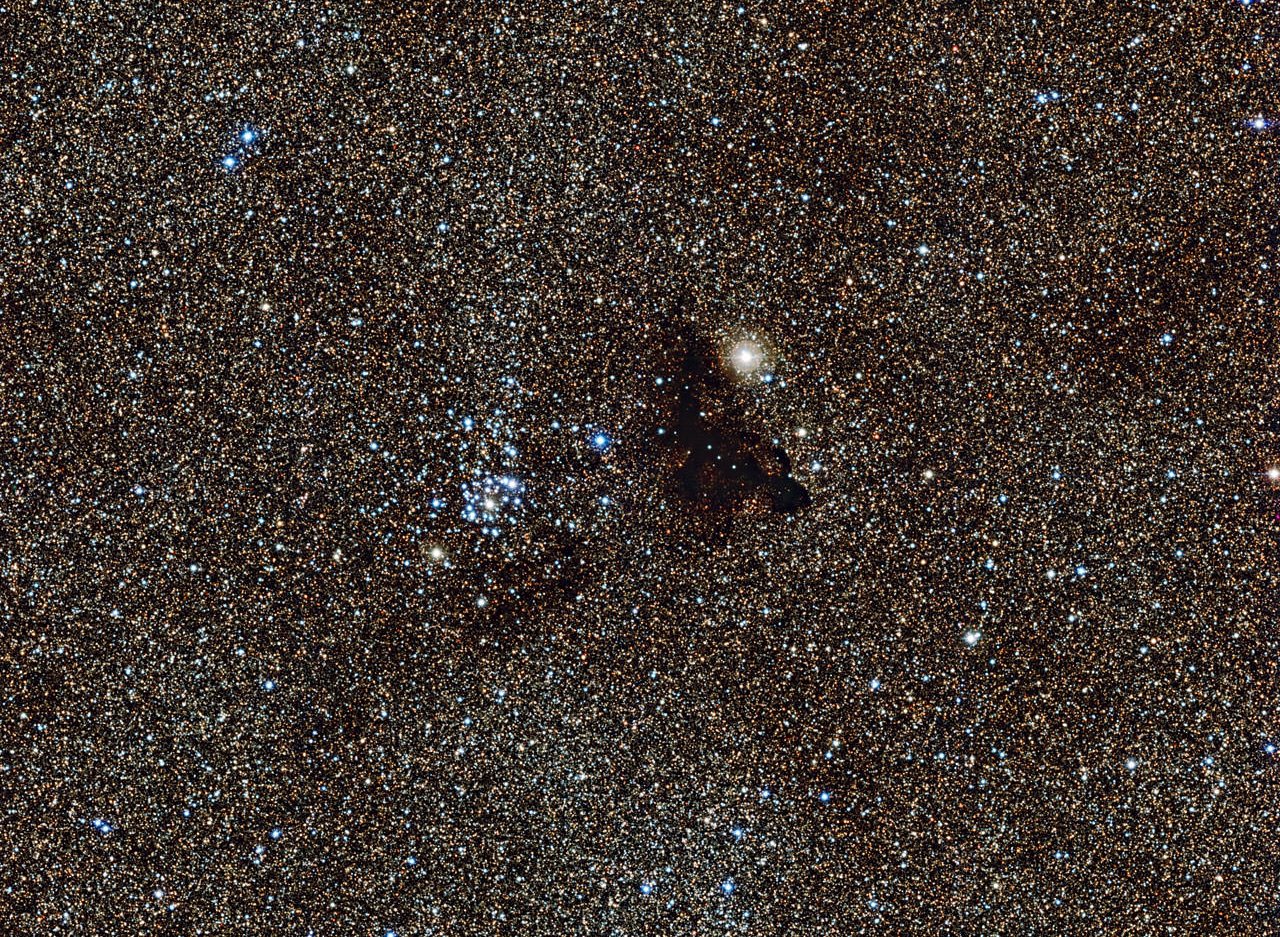 This image from the Wide Field Imager on the MPG/ESO 2.2-metre telescope at ESO’s La Silla Observatory in Chile, shows the bright star cluster NGC 6520 and its neighbour, the strangely shaped dark cloud Barnard 86. This cosmic pair is set against millions of glowing stars from the brightest part of the Milky Way — a region so dense with stars that barely any dark sky is seen across the picture.