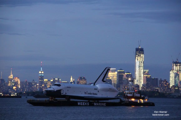 NASA’s real life Space Shuttle Enterprise transits the NYC Skyline at Dusk on a barge on June 3, 2012 during a two stage seagoing  journey to her permanent  new home at the Intrepid Sea, Air and Space Museum. Enterprise is bracketed by the Empire State Building, The Freedom Tower (still under construction) and the torch lit Statue of Liberty. Credit: Ken Kremer