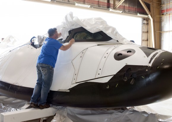 A Sierra Nevada employee removes plastic wrapping from Dream Chaser after it arrives at NASA's Dryden Flight Research Center in southern California. Credit: NASA
