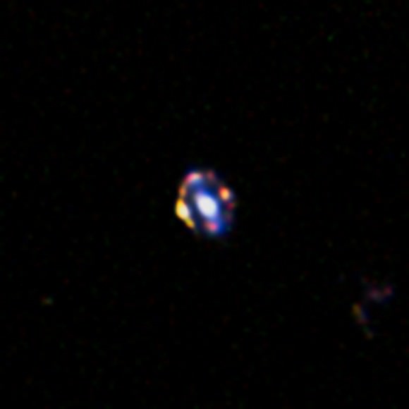 A picture of the object J1000+0221, which demonstrates the most distant gravitational lens ever discovered. This Hubble picture shows a normal galaxy's center region (the glow in the picture), but the object is also aligned with a younger, star-creating galaxy that is in behind. The object in the foreground pulls light from the background galaxy with gravity -- making rings of  pictures. Credit: NASA/ESA/A. van der Wel