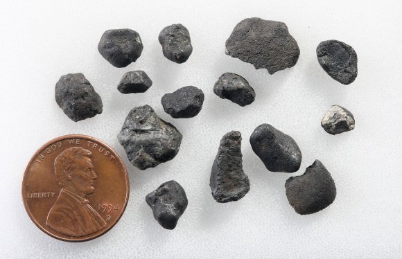 Friction and enormous pressures placed upon the Chelyabinsk meteoroid by the atmosphere caused it to explode to pieces and send a shock wave across the cities below. This is a selection of typical small, fusion-crust covered Chelyabinsk meteorites. The U.S. penny is 9mm in diameter. Credit: Bob King