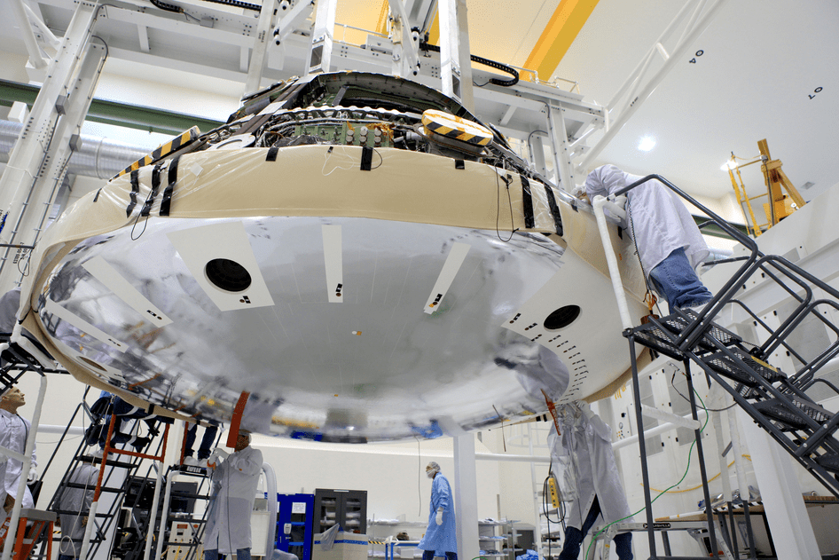 Orion heat shield attached to the bottom of the capsule by engineers during assembly work inside the  Operations and Checkout High Bay facility at KSC. Credit: NASA