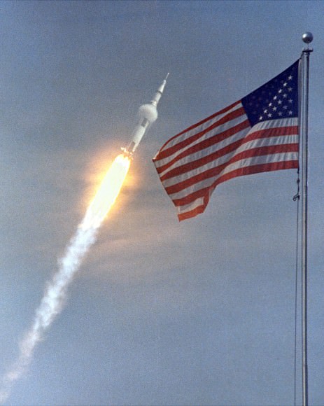 Apollo 11 Launch.  The American flag heralded the launch of Apollo 11, the first Lunar landing mission, on July 16, 1969. The massive Saturn V rocket lifted off from NASA's Kennedy Space Center with astronauts Neil A. Armstrong, Michael Collins, and Edwin "Buzz" Aldrin at 9:32 a.m. EDT. Four days later, on July 20, Armstrong and Aldrin landed on the Moon's surface while Collins orbited overhead in the Command Module. Armstrong and Aldrin gathered samples of lunar material and deployed scientific experiments that transmitted data about the lunar environment.   Credit: NASA