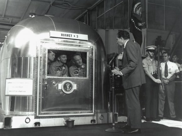 President Nixon Greets the Returning Apollo 11 Astronauts. The Apollo 11 astronauts, left to right, Commander Neil A. Armstrong, Command Module Pilot Michael Collins and Lunar Module Pilot Edwin E. "Buzz" Aldrin Jr., inside the Mobile Quarantine Facility aboard the USS Hornet, listen to President Richard M. Nixon on July 24, 1969 as he welcomes them back to Earth and congratulates them on the successful mission. The astronauts had splashed down in the Pacific Ocean at 12:50 p.m. EDT about 900 miles southwest of Hawaii.  Credit: NASA