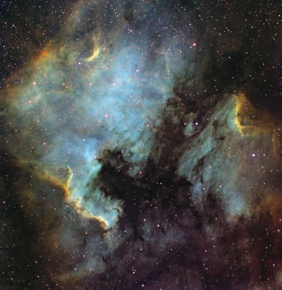 This false color image of the North America and Pelican nebulae covers 3° and shows the SII, Hydrogen Alpha, and OIII lines isolated with a set of 3 nm wide narrowband filters using a CCD camera from a very light-polluted area, with cumulative exposure times of 12, 2.5, and 4.5 hours respectively. Each 5-minute raw frame was calibrated and all of them were registered. Then, each stacked group was assigned to a layer in the MaxIm DL Combine Color function in LRGB mode: H? to luminance and green, SII to red, and OIII to blue. To compensate for the weakness of OIII, and especially SII with regard to H a, their respective amplification factors were 3.5 and 10. Final adjustment of levels, curves, and color saturation was done using Photoshop after export from MaxIm DL in 16-bit TIFF format. Credit and copyright: Thierry Legault. 