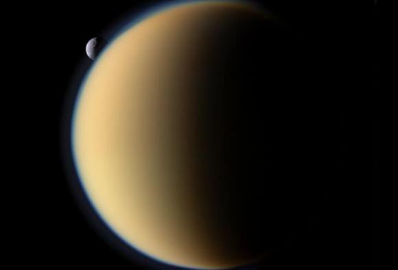 Saturn's moon Titan with Tethys hovering in the background. Image taken by the Cassini spacecraft. Credit: NASA/JPL/Space Science Institute