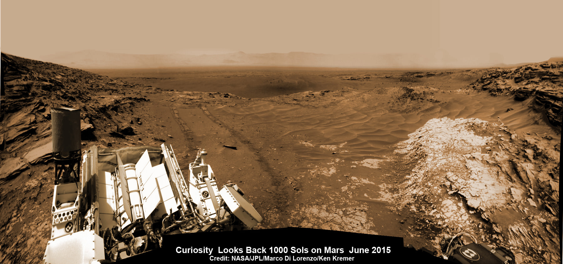 NASA’s Martian Curiosity rover looks backs to 1000 Sols of science and exploration on the surface of the Red Planet.  Robot wheel tracks lead back through valley dunes.  Gale Crater rim seen in the distant hazy background.  Sol 997 (May 28, 2015) navcam camera raw images stitched and colorized. Credit:  NASA/JPL-Caltech/ Marco Di Lorenzo/Ken Kremer/kenkremer.com Featured on APOD on June 13, 2015