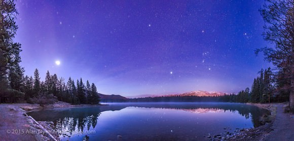 A panorama of roughly 120° showing a star- and planet-filled sky in the dawn twilight over Lake Annette in Jasper National Park, Alberta, on the morning of October 25, 2015.   At left, to the east, are the two bright planets, Venus (brightest) and Jupiter in a close conjunction 1° apart (and here almost merging into one glow), plus reddish Mars below them, all in Leo, with the bright star Regulus above them. Right of centre, to the south, is Orion and Canis Major, with the bright star Sirius low in the south. At upper right are the stars of Taurus, including Aldebaran and the Hyades star cluster. Venus was near greatest elongation on this morning. Credit and copyright: Alan Dyer. 