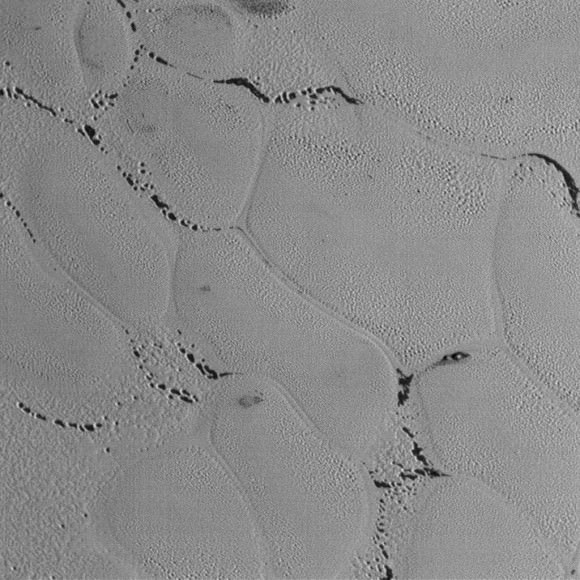 This wider view shows the textured surface of Pluto's icy plains riddled with small pits. It almost looks like the dark areas in the sinuous channels between the mounds were once covered with frost or ice that has since sublimated away. They look similar to the polar regions on Mars where carbon dioxide frost burns off in the spring to reveal darker material beneath. Credit: NASA/JHUAPL/SwRI