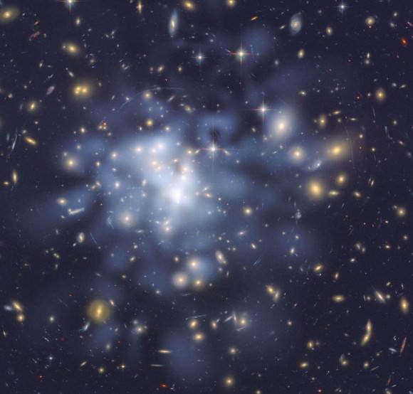 This NASA Hubble Space Telescope image shows the distribution of dark matter in the center of the giant galaxy cluster Abell 1689, containing about 1,000 galaxies and trillions of stars. Researchers used the observed positions of 135 lensed images of 42 background galaxies to calculate the location and amount of dark matter in the cluster. They superimposed a map of these inferred dark matter concentrations, tinted blue, on an image of the cluster taken by Hubble