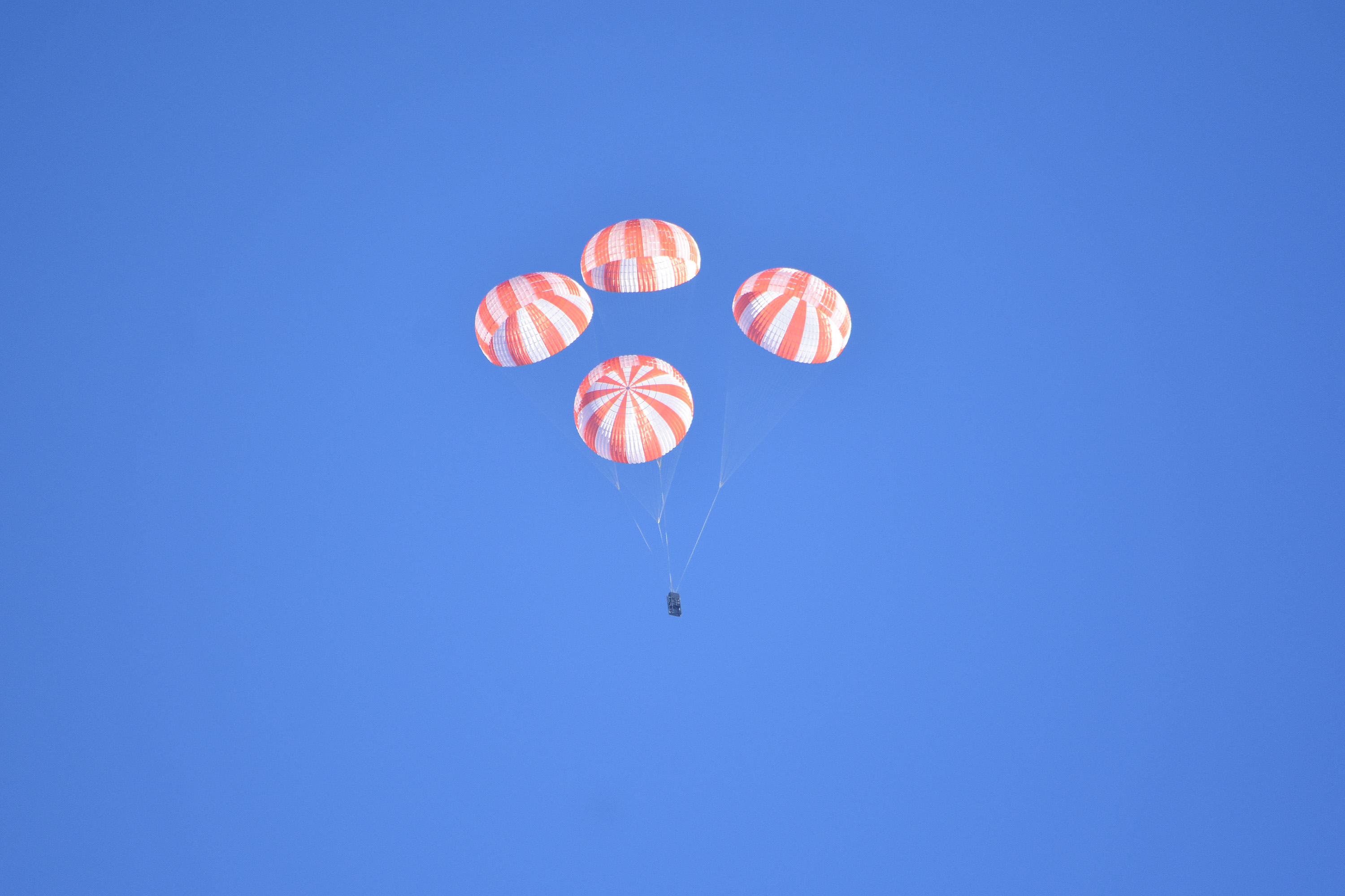 Parachute drop test for SpaceX crew Dragon involving  four red-and-white parachutes unfurled from a mass simulator high above the desert near Coolidge, Arizona. Credit NASA/SpaceX