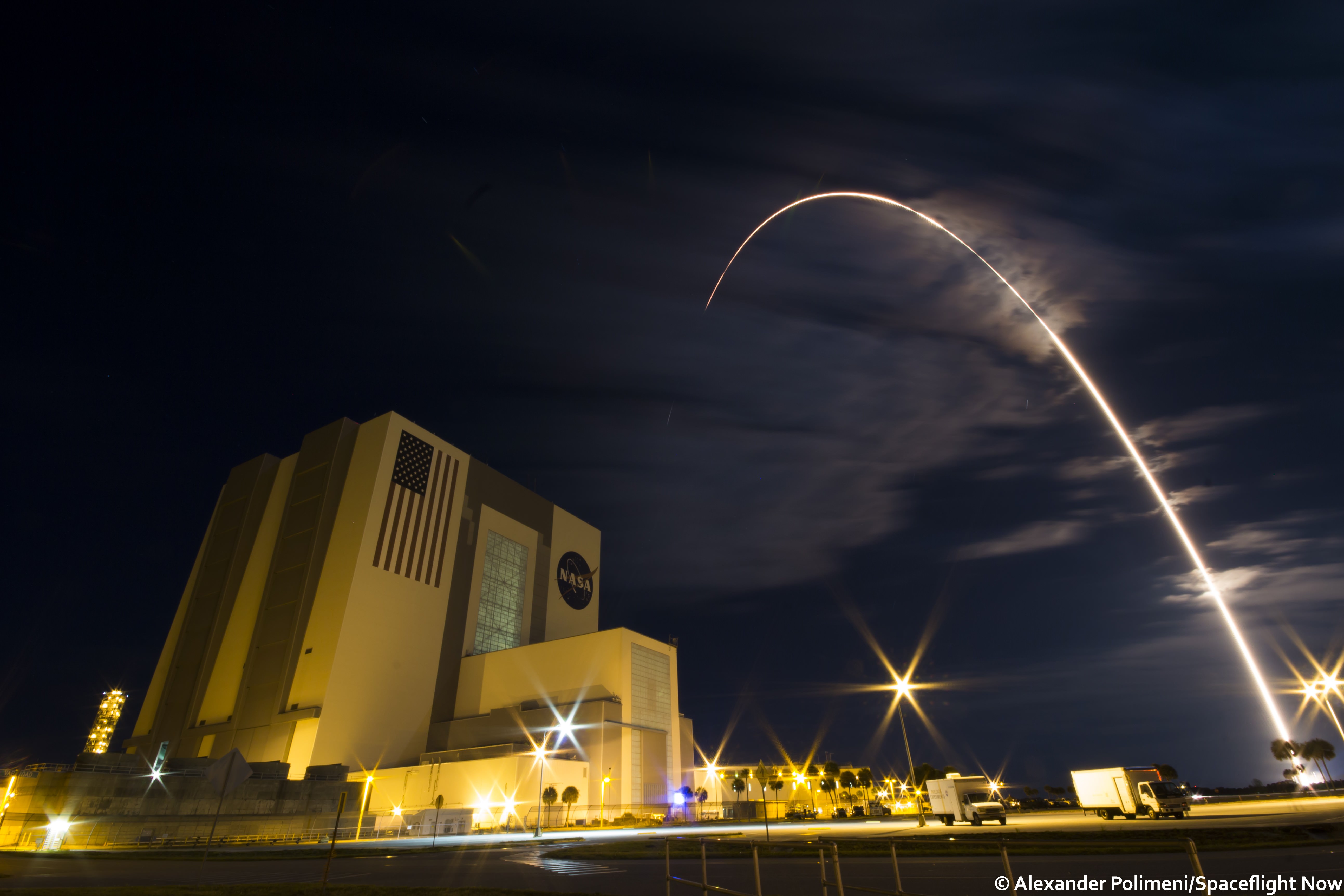 Long exposure streak shot of blastoff of United Launch Alliance Atlas V rocket carrying Orbital ATK's Cygnus spacecraft at 11:05 p.m. EDT on March 22, 2016, with foreground view of world famous Vehicle Assembly Building (VAB) at NASA’s Kennedy Space Center in Florida.  Atlas V lifted off from nearby Space Launch Complex 41 on Cape Canaveral Air Force Station in Florida. Credit: Alex Polimeni/Spaceflight Now 