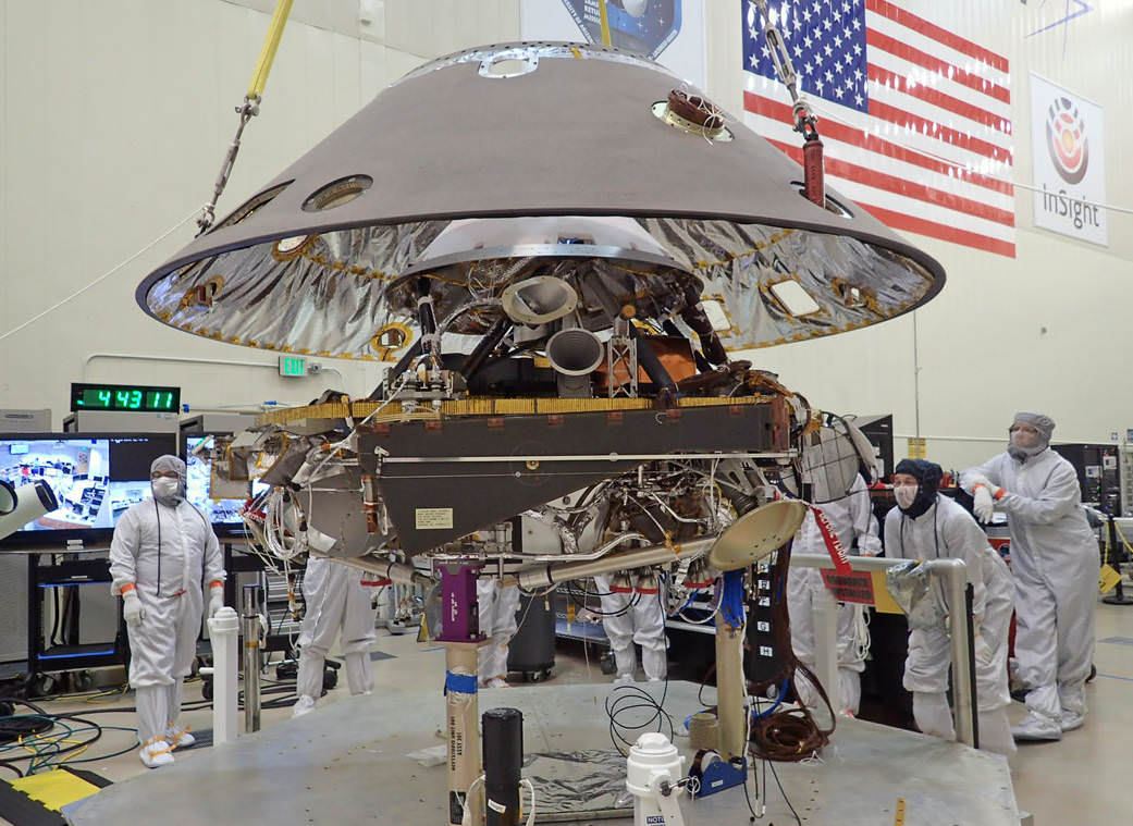 Back shell of NASA's InSight spacecraft is being lowered onto the mission's lander, which is folded into its stowed configuration.  The back shell and a heat shield form the aeroshell, which will protect the lander as the spacecraft plunges into the upper atmosphere of Mars.  Launch now rescheduled to May 2018 to fix French-built seismometer.  Credit: NASA/JPL-Caltech/Lockheed Martin 
