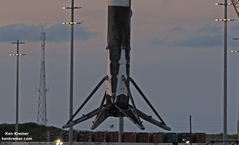 With US flag flying in background below, the base of recovered SpaceX Falcon 9 booster with 4 deployed landing legs and 9 Merlin 1 D engines is lifted off ‘OCISLY’ droneship barge at dusk on June 2, 2016 after sailing at  midday through Port Canaveral. The rocket  successfully launched Thaicom-8 satellite on May 27, 2016 from Cape Canaveral Air Force Station, Fl and landed on sea based platform minutes later.  Credit: Ken Kremer/kenkremer.com