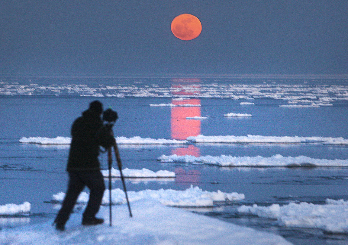 A photographer finds just the right spot in Duluth along Lake Superior to photograph the Full Moon rise. The flattened shape of the Moon is caused by the layer of denser air closer to the horizon refracting or bending the bottom half of the Moon more strongly than the thinner air n