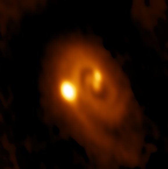 ALMA image of the L1448 IRS3B system, with two young stars at the center and a third distant from them. Spiral structure in the dusty disk surrounding them indicates instability in the disk, astronomers said. Credit: Bill Saxton, ALMA (ESO/NAOJ/NRAO), NRAO/AUI/NSF