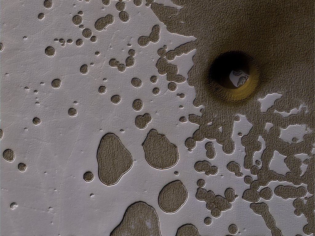 The HiRISE camera on NASA's Mars Reconnaissance Orbiter captured this unusual crater or pit on the surface of Mars. Frozen carbon dioxide gives the region its unique "Swiss cheese" like appearance. Image:NASA/JPL/University of Arizona