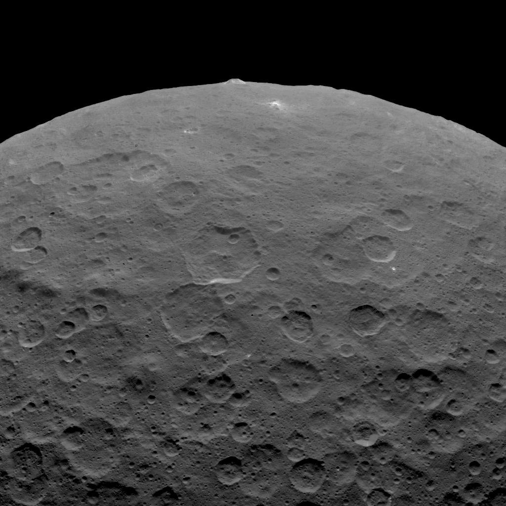 The 4 km high ice volcano Ahuna Mons (top) is visible projecting above the cratered surface of the dwarf planet Ceres. Image: By NASA/JPL-Caltech/UCLA/MPS/DLR/IDA