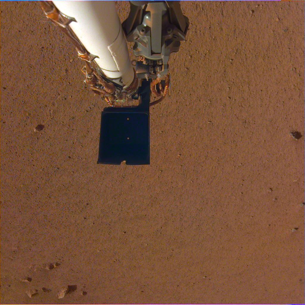 This image was captured by InSight's Instrument Deployment Camera taken while the camera still had its transparent protective dust cover in place. It shows the grapple in stowed position, and the dark scoop at the end of the arm. The five-fingered grapple is used to deploy the instruments on the Martian surface. Image: NASA/JPL-Caltech