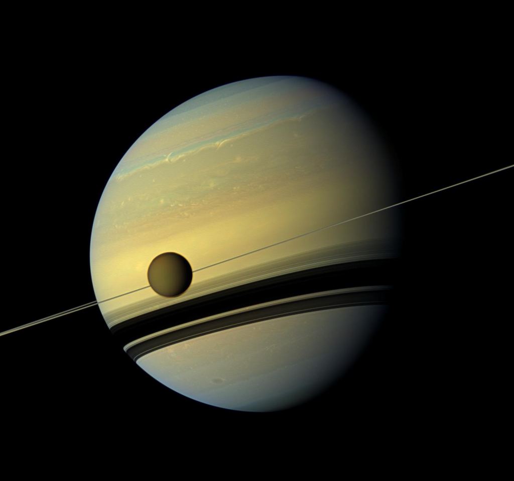 This image shows Titan in front of Saturn. Several of Saturn's moons are shepherd moons that help keep the planet's ring structure stable. Image Credit: NASA/JPL-Caltech/Space Science Institute