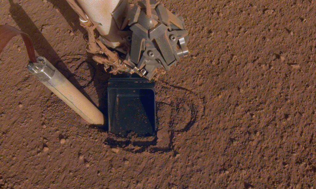 This image shows the difficulty that InSight's Heat Probe (HP3) faced. Due to the nature of Martian regolith, it kept popping out of its hole. In this image, mission operators tried using the lander's scoop to press on the probe's hole. They hoped that would provide the friction necessary for the hammering action to be effective. Image Credit: NASA/JPL-Caltech