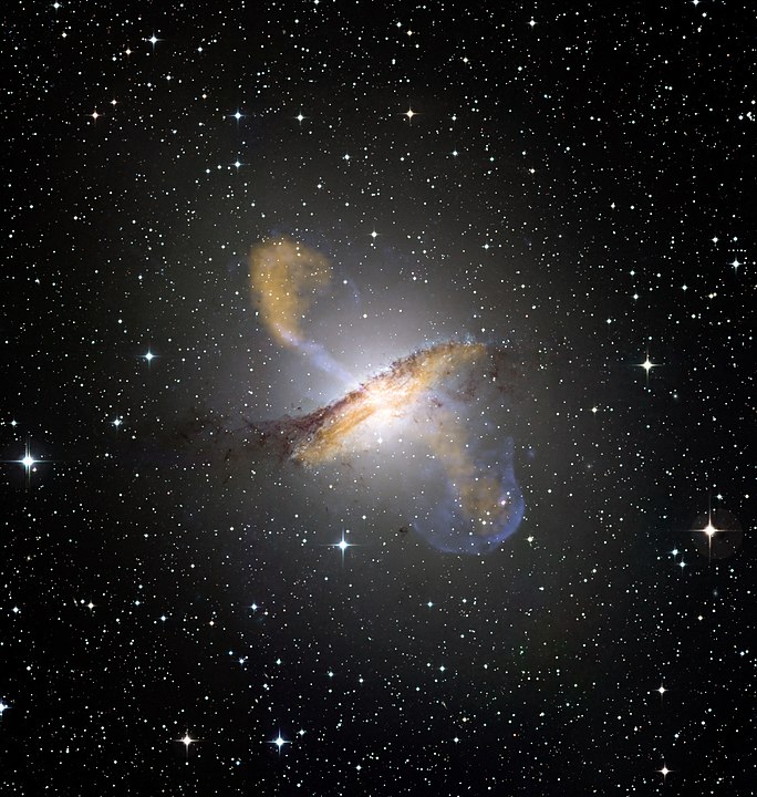 Colour composite image of Centaurus A, revealing the lobes and jets emanating from the active galaxy’s central black hole. This is a composite of images obtained with three instruments, operating at very different wavelengths. The 870-micron submillimetre data, from LABOCA on APEX, are shown in orange. X-ray data from the Chandra X-ray Observatory are shown in blue. Visible light data from the Wide Field Imager (WFI) on the MPG/ESO 2.2 m telescope located at La Silla, Chile, show the stars and the galaxy’s characteristic dust lane in close to "true colour". By ESO/WFI (Optical); MPIfR/ESO/APEX/A.Weiss et al. (Submillimetre); NASA/CXC/CfA/R.Kraft et al. (X-ray) - http://www.eso.org/public/images/eso0903a/, CC BY 4.0, https://commons.wikimedia.org/w/index.php?curid=5821706