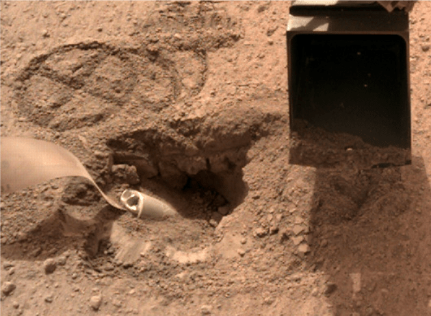 This image, acquired on Sol 577, shows the Mole almost completely covered with sand. It also shows the footprint of the scoop in front of the Mole on the near side and interesting overhangs and layers in the duricrust on the far side. The overhang does not necessarily define the thickness of the duricrust but may indicate layering in the latter. The overhang has regular spaced cracks that are astoundingly wide. The horizon above the cracked crust may indicate the bottom of a near surface sand layer. Image Credit: NASA/JPL-Caltech.