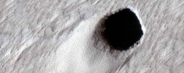 A collapsed section of the ceiling of a lava tube on Mars. This pit crater is 50 m (150 ft) across, and is on the flank of the extinct volcano Arsia Mons. Image Credit: NASA/JPL/University of Arizona