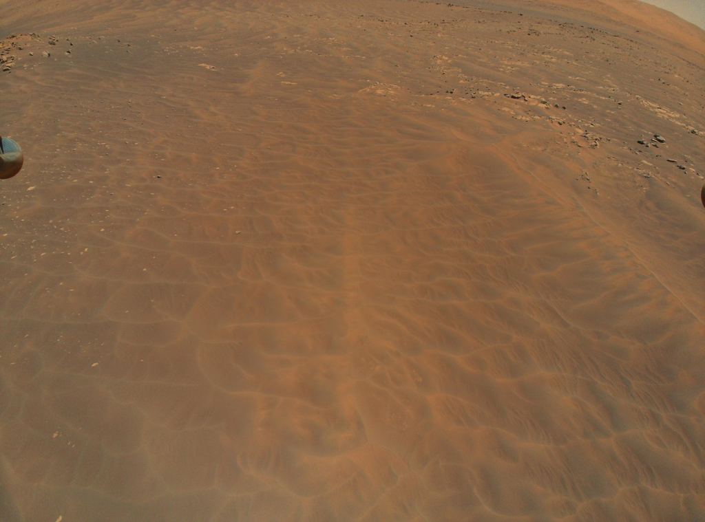 Ingenuity's view of the Séítah dune field on it's ninth flight.  Part of the helicopter's landing gear can be seen on the left side of the screen.