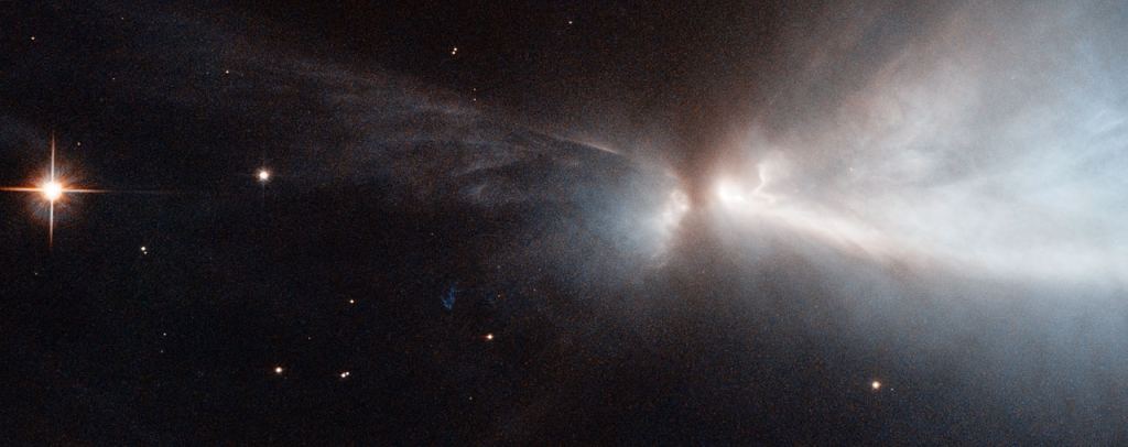 This striking new image, captured by the NASA/ESA Hubble Space Telescope, reveals a newly forming starwithin the Chamaeleon cloud in the Milky Way. This young star is throwing off narrow streams of gas from its poles — creating this ethereal object known as HH 909A. These speedy outflows collide with the slower surrounding gas, lighting up the region. When new stars form, they gather material hungrily from the space around them. A young star will continue to feed its huge appetite until it becomes massive enough to trigger nuclear fusion reactions in its core, which light the star up brightly. Before this happens, new stars undergo a phase during which they violently throw bursts of material out into space. This material is ejected as narrow jets that streak away into space at breakneck speeds of hundreds of kilometres per second, colliding with nearby gas and dust and lighting up the region. The resulting narrow, patchy regions of faintly glowing nebulosity are known as Herbig-Haro objects. They are very short-lived structures. These structures are very common within star-forming regions like the Orion Nebula, or the Chameleon I molecular cloud. 