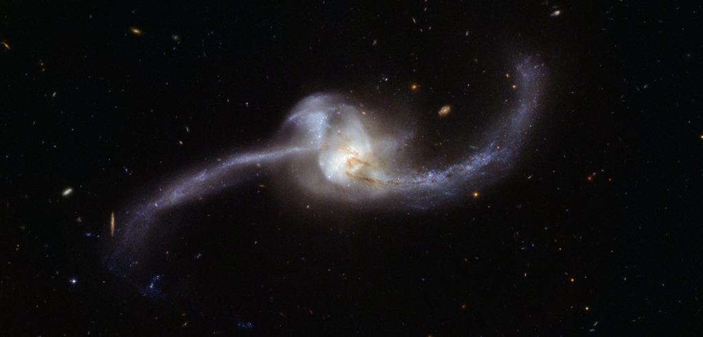 Ini adalah gambar teleskop Hubble dari NGC 2623, penggabungan tahap akhir antara dua galaksi spiral.  Penggabungan memampatkan gas di kedua galaksi memicu lonjakan pembentukan bintang aktif.  Tetapi beberapa galaksi jauh mengalami pembentukan bintang yang intens yang tidak dipicu oleh penggabungan, dan sulit untuk membedakan keduanya.  Kredit Gambar: Oleh ESA/Hubble, CC BY 4.0, https://commons.wikimedia.org/w/index.php?curid=63401428 