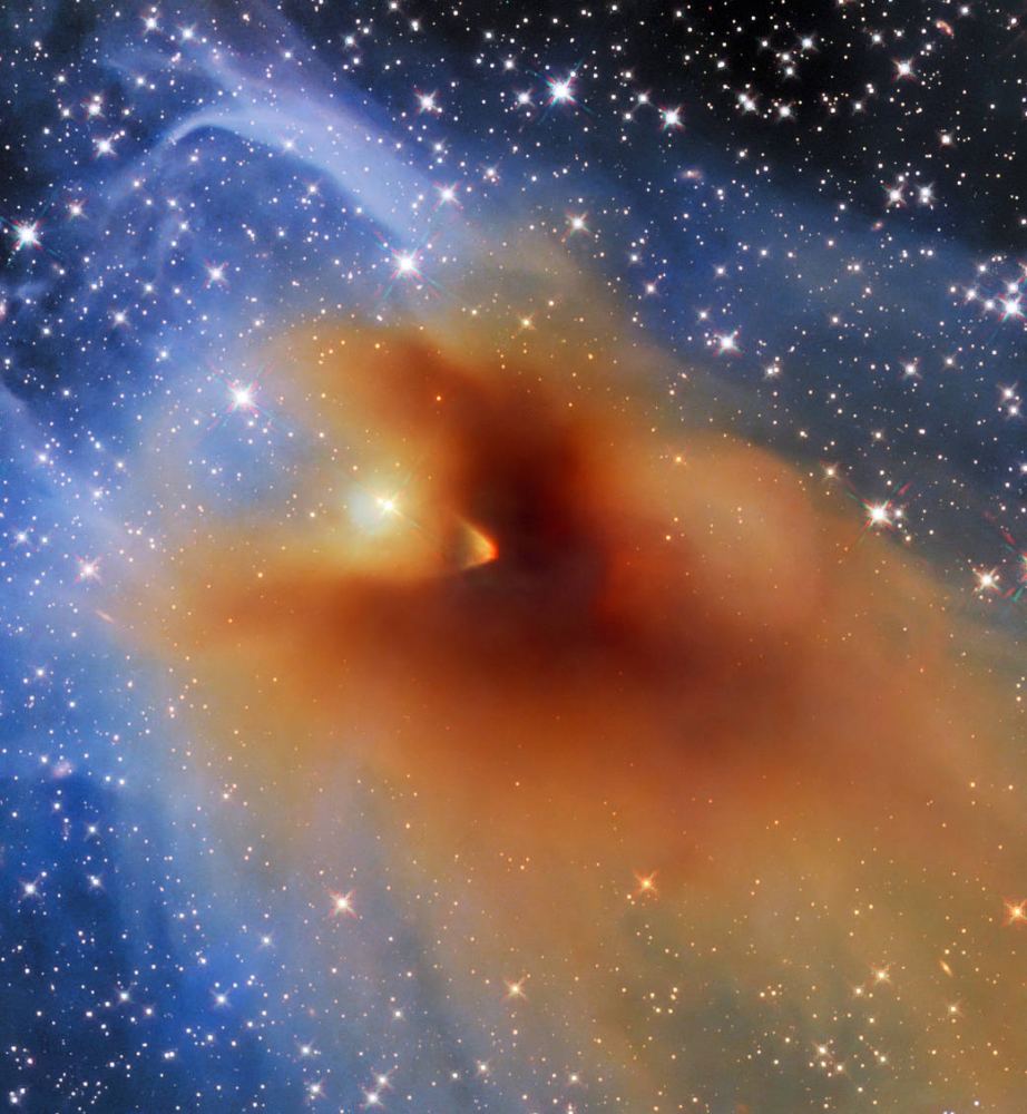 A small, dense cloud of gas and dust called CB 130-3 blots out the center of this image from the NASA/ESA Hubble Space Telescope.