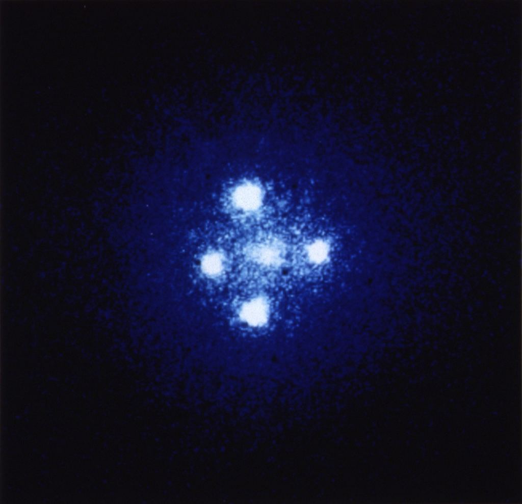 A gravitational lens caused by a galaxy in the foreground leading to an "Einstein Cross." Credit: NASA/ESA/STScI