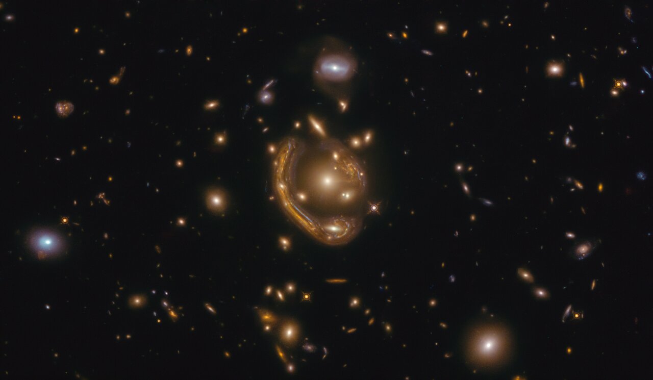 The narrow galaxy elegantly curving around its spherical companion in this image is a fantastic example of a truly strange and very rare phenomenon. This image, taken with the NASA/ESA Hubble Space Telescope, depicts GAL-CLUS-022058s, located in the southern hemisphere constellation of Fornax (The Furnace). GAL-CLUS-022058s is the largest and one of the most complete Einstein rings ever discovered in our Universe. The object has been nicknamed by the Principal Investigator and his team who are studying this Einstein ring as the "Molten Ring", which alludes to its appearance and host constellation. First theorised to exist by Einstein in his general theory of relativity, this object’s unusual shape can be explained by a process called gravitational lensing, which causes light shining from far away to be bent and pulled by the gravity of an object between its source and the observer. In this case, the light from the background galaxy has been distorted into the curve we see by the gravity of the galaxy cluster sitting in front of it. The near exact alignment of the background galaxy with the central elliptical galaxy of the cluster, seen in the middle of this image, has warped and magnified the image of the background galaxy around itself into an almost perfect ring. The gravity from other galaxies in the cluster is soon to cause additional distortions. Objects like these are the ideal laboratory in which to research galaxies too faint and distant to otherwise see.