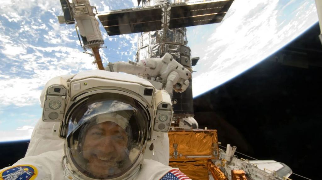 This image shows astronaut Mike Massimino during Service Mission 4 to the Hubble in 2009. Astronaut Mike Good is in the background. During SM-4, Hubble received new gyroscopes, as well as two new scientific instruments – the Cosmic Origins Spectrograph (COS) and Wide Field Camera 3 (WFC3). Image Credit: NASA
